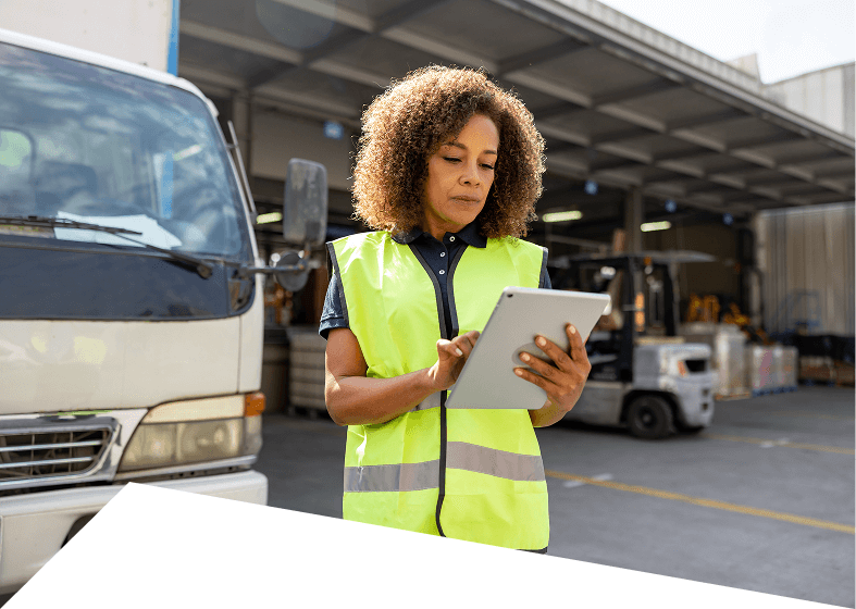 Woman in safety vest using tablet outdoors.