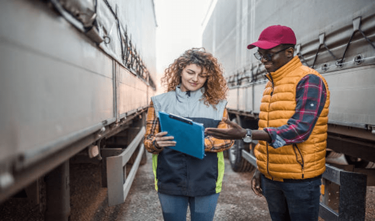 Two logistics workers discussing documents between trucks.