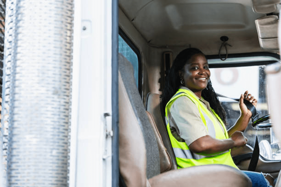 Smiling woman in safety vest sitting in a vehicle cabin.